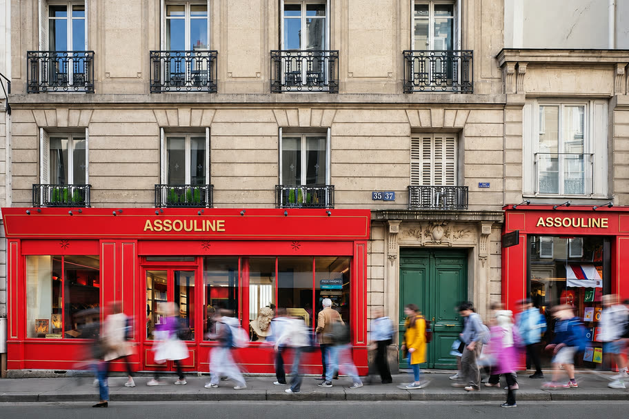 Passers-by blurring along the red Assouline storefront on a Paris street